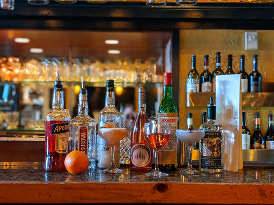 A image of the Mambo bar counter. Various liqueurs and types of glasses. Upside down wine glasses hanging above are reflected in the bar mirror in the background.