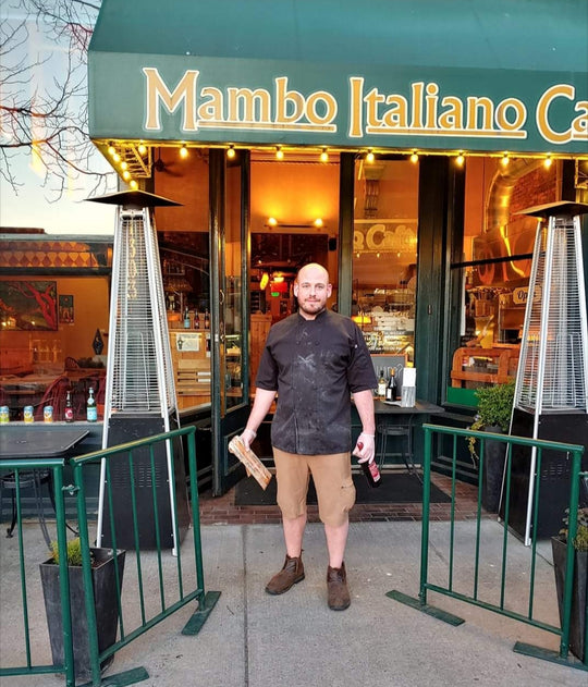 Restaurant owner Dom Tino standing in front of the Mambo storefront in a chef's jacket. 