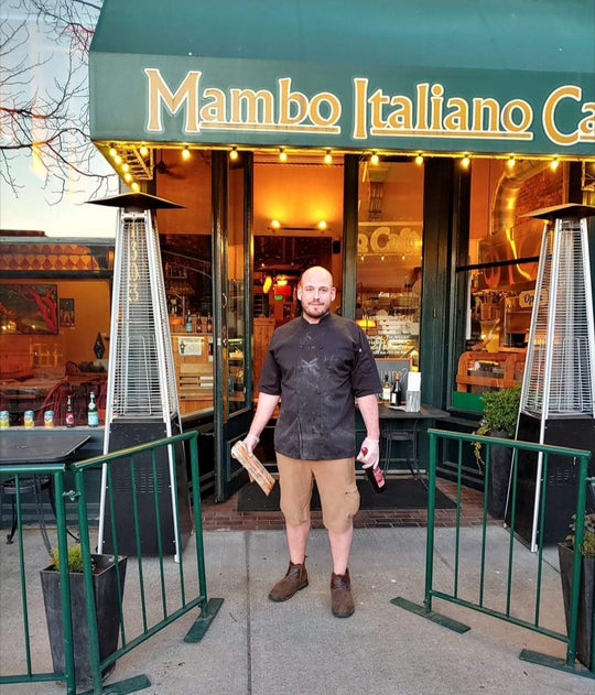 Restaurant owner Dom Tino standing in front of the Mambo storefront in a chef's jacket.