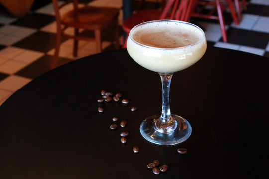A coup glass with Mambo's espresso martini on a black table with coffee beans scattered. 