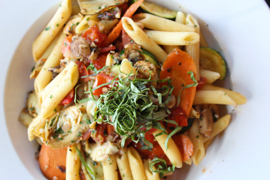 Penne Primavera: Penne noodles tossed with bright orange carrots, zucchini, brown crimini mushrooms, and a finely sliced basil garnish 