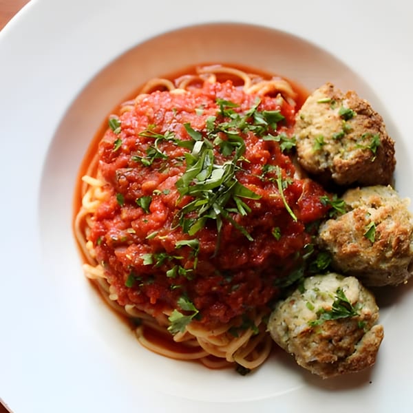 Spaghetti with chunky red tomato sauce and three large meatballs, garnished with fresh herbs.