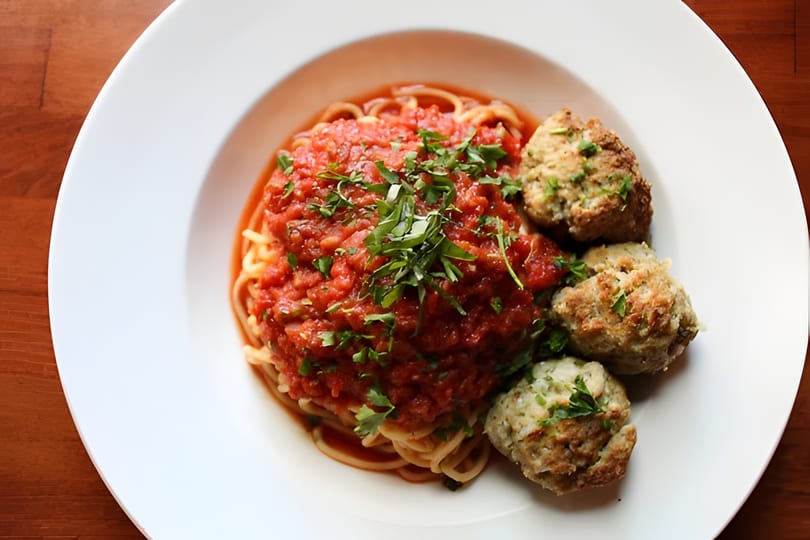Spaghetti with chunky red tomato sauce and three large meatballs, garnished with fresh herbs.