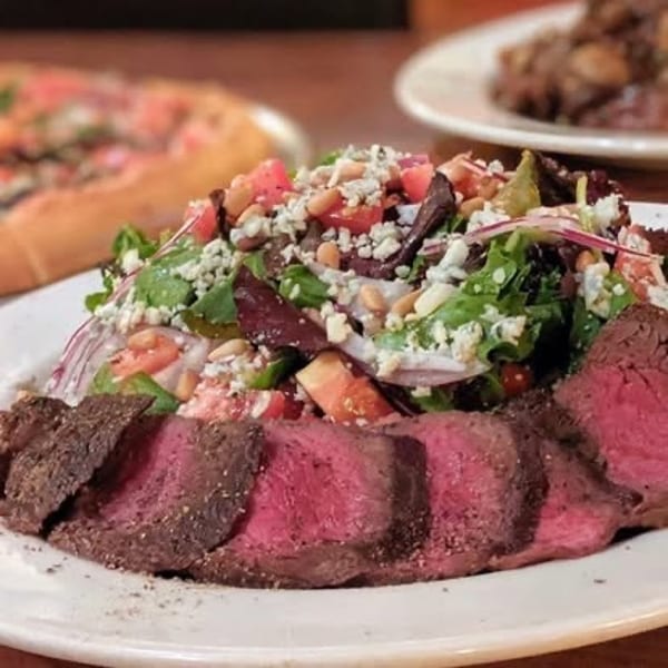 Sliced medium-rare steak served with a fresh salad topped with blue cheese and pine nuts.