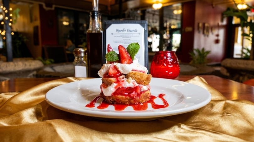 Strawberry shortcake dessert with whipped cream and mint on a white plate with a gold tablecloth.