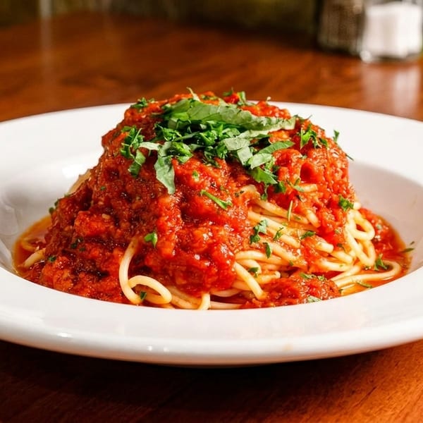 Spaghetti with rich red tomato sauce and fresh green herbs in a white bowl on a wooden table.
