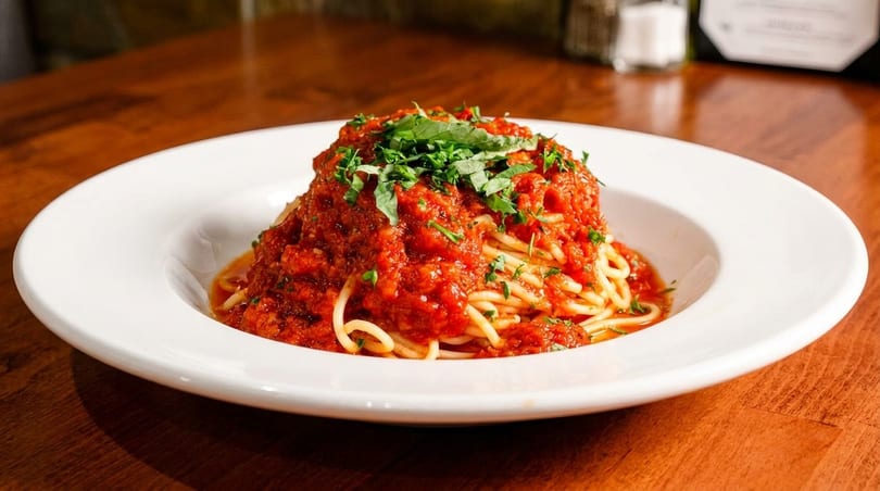 Spaghetti with rich red tomato sauce and fresh green herbs in a white bowl on a wooden table.