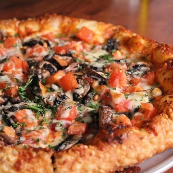 Close-up of a freshly baked pizza with tomatoes, mushrooms, melted cheese, and a crispy crust.