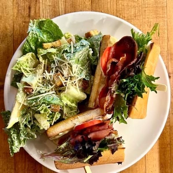 Caesar salad and a bacon, lettuce, tomato sandwich on a white plate.